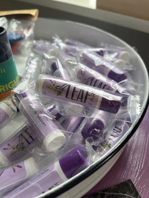 A pile of Elf Leaf Farm lip balms. Each lip balm is individually packaged and has a purple label. 