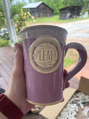 A hand holding a purple ceramic mug with the Elf Leaf Farm logo.