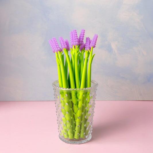 Lavender-shaped pens sit in a glass cup. 